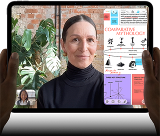 iPad Pro, front exterior, landscape orientation, space black color, rounded corners, black display bezel, hands holding left and right sides, display showing a FaceTime conversation being live translated, and an educational app showing a presentation of "Comparative Mythology" with text, diagrams, and handwritten notes